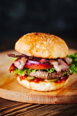 Burger pastırma, et, domates ve marul üzerine ahşap arka plan ile. Yakın çekim. Kopya alanı