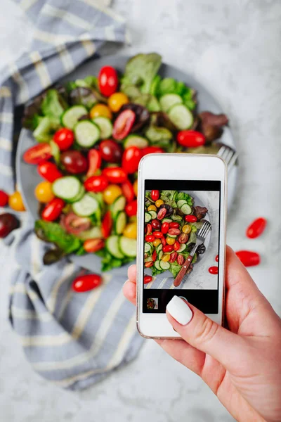 Wanita yang memegang ponsel dan memotret salad tomat ceri merah dan kuning — Stok Foto