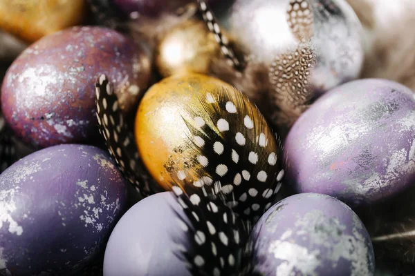 Violet, gold and silver easter eggs and beautiful decorative feathers close up