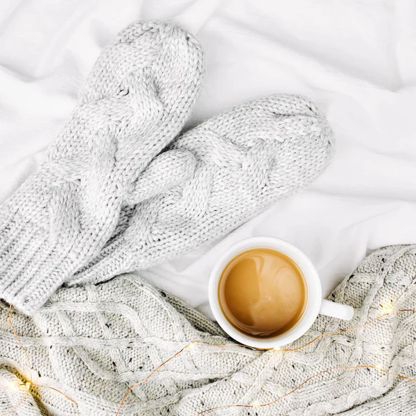 Cup of coffee on bed with warm plaid and mittens