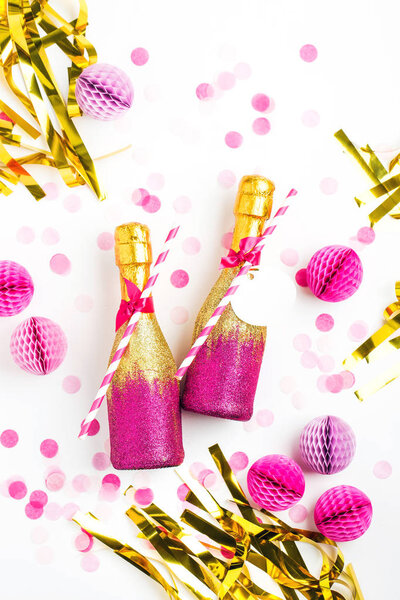 two champagne bottles decorated in pink and golden glitter, golden tinsel and pink paper balls 