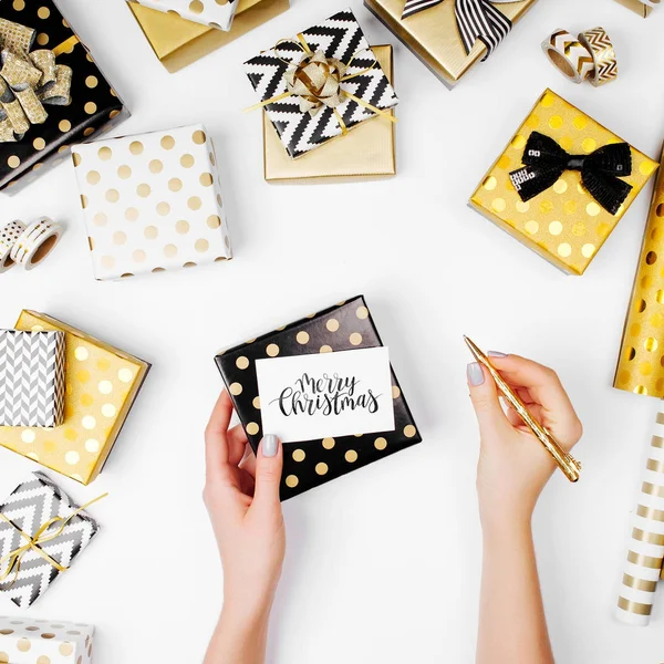 手持圣诞贺卡的女性手 金黄礼物和包装纸的平的放置在背景 — 图库照片