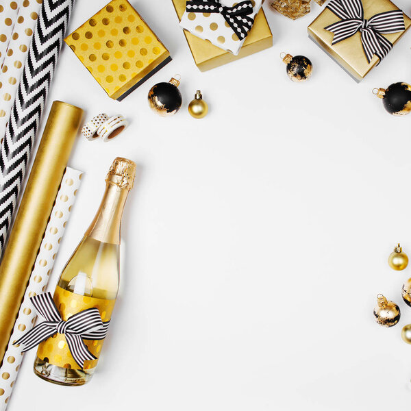 flat lay of champagne bottle, presents and golden wrapping paper rolls on white background