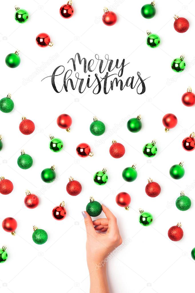 female hand making pattern of red and green Christmas balls on white background. Merry Christmas text 