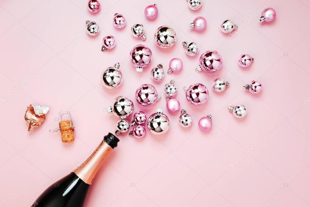 champagne bottle and shiny Christmas balls on pink background, top view