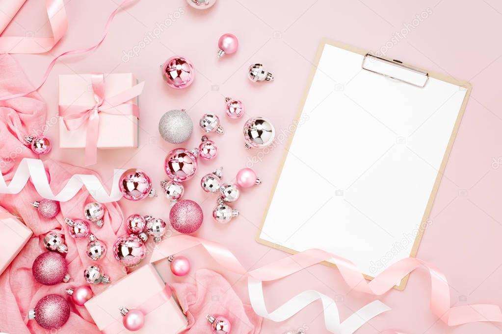 Flat Lay Holiday Background with blank clipboard, Christmas balls, ribbons and gifts in pink colour