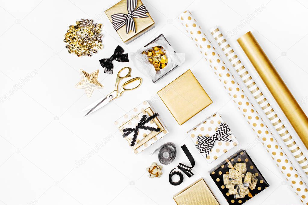 flat lay of golden presents, wrapping paper and decorations on white background 