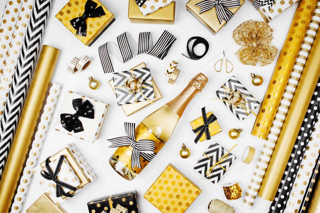 flat lay of champagne bottle, presents and golden wrapping paper rolls on white background