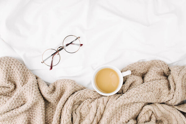 Cup of hot coffee wrapped in plaid, placed on bed sheets with glasses