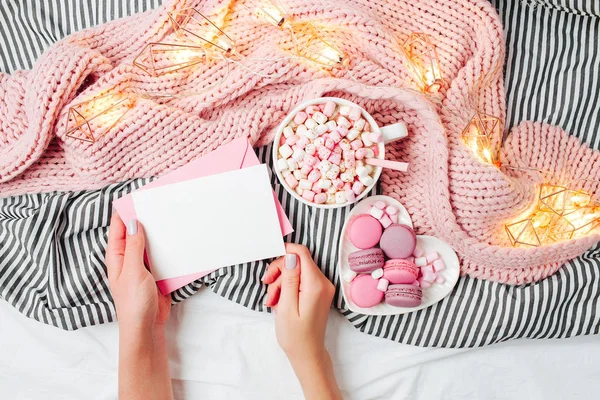 Top view of hands with letter, cup of coffee with marshmallows, cookies and fairy lights