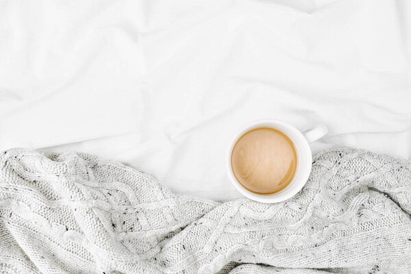 Cup of hot coffee wrapped in plaid, placed on bed sheets 