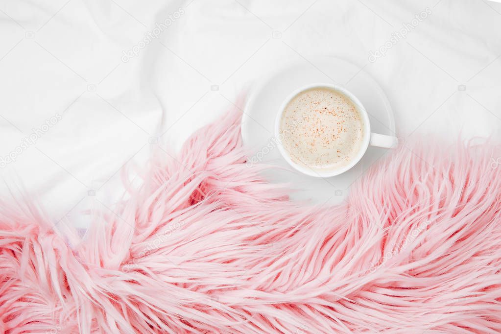Top view of cup of coffee and pink fluffy fur plaid a pink fluffy fur plaid on bedding sheet