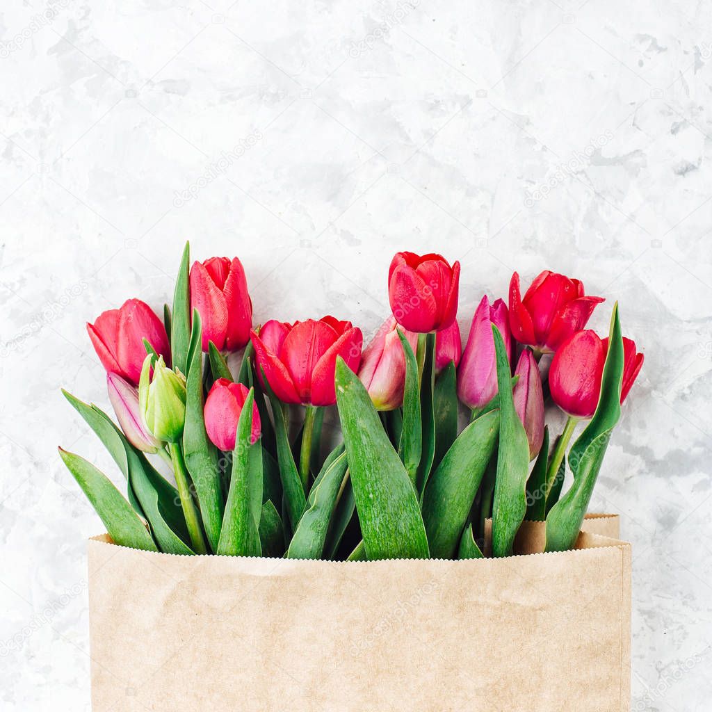 Bouquet of tulips in paper kraft paper bag on grey background