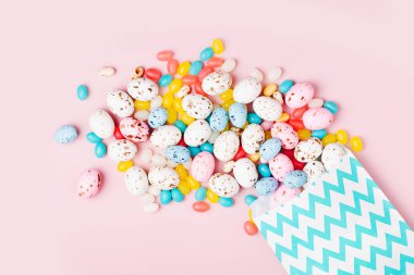 Şeker çikolata yumurta ve parti kağıt çanta pembe bir arka plan üzerinde üzerinden akan Jellybean