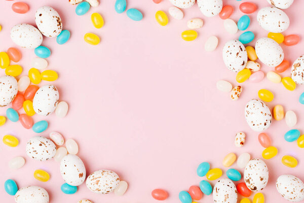 Stylish frame made of Easter candy chocolate eggs and Jellybean on pink background