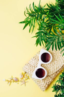 Tropikal yaprak ve plaj çantası Sarı zemin üzerine güneş gözlüklü. Üstten Görünüm, düz yatıyordu.