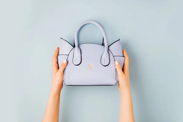 Female hands holds handbag on blue background . Flat lay, top view. Spring fashion concept in pastel colored