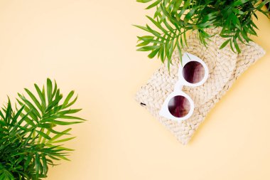 Tropikal yaprak ve plaj çantası Sarı zemin üzerine güneş gözlüklü. Üstten Görünüm, düz yatıyordu.