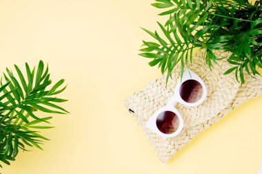 Tropikal yaprak ve plaj çantası Sarı zemin üzerine güneş gözlüklü. Üstten Görünüm, düz yatıyordu.