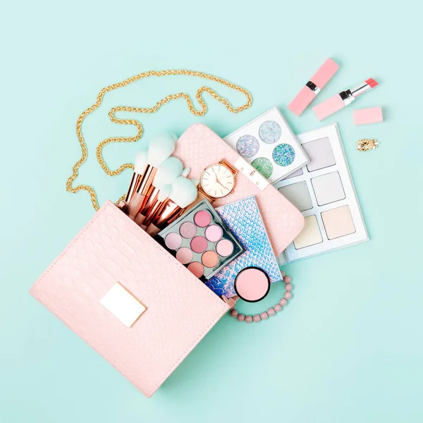 Cosmetic products flowing from Makeup bag on pastel blue background.  Flat lay, top view. Fashion concept