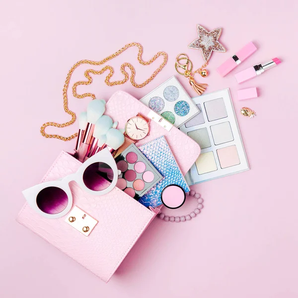 Cosmetic products flowing from Makeup bag on pastel pink background.  Flat lay, top view. Fashion concept