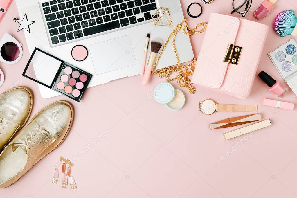 Fashion blogger workspace with laptop and female accessory, cosmetics products on pale pink table. flat lay, top view