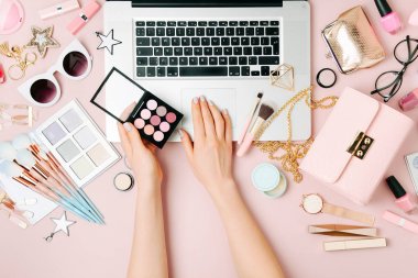 Kadın moda blogger ile dizüstü bilgisayar aksesuarları, kozmetik ürünleri ile çalışma alanı çalışma görünümünü kırpılmış.
