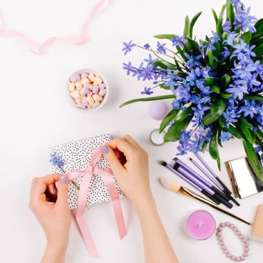 Arka planda mavi bahar buket, kahve, şeker ve kozmetik aksesuarlar ile hediye açmak eller.