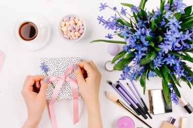 Arka planda mavi bahar buket, kahve, şeker ve kozmetik aksesuarlar ile hediye açmak eller.