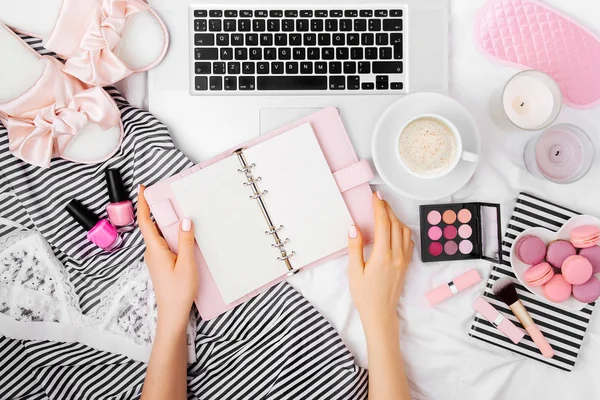 Fashion blogger working with laptop and planner in bed and drinking coffee.