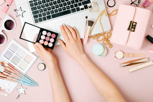 Cropped view of female fashion blogger working with laptop on workspace with accessories, cosmetics products.