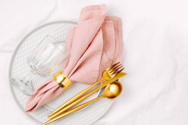 Festival sofra cam plakanın ve beyaz arka plan üzerinde pembe peçete ile altın çatal bıçak takımı. 