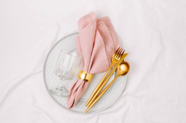 Festival sofra cam plakanın ve beyaz arka plan üzerinde pembe peçete ile altın çatal bıçak takımı. 