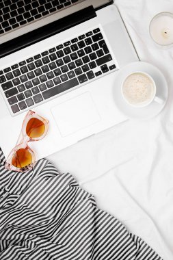 Yatakta laptop, güneş gözlüğü ve sabah kahve ile moda blogger çalışma alanı.