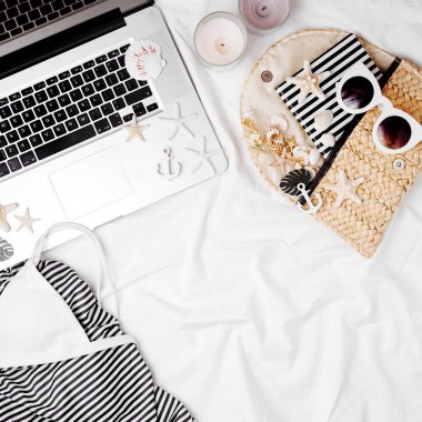 Güneş gözlüğü ve yatakta aksesuarları ile dizüstü bilgisayar, mayo ve plaj çantası