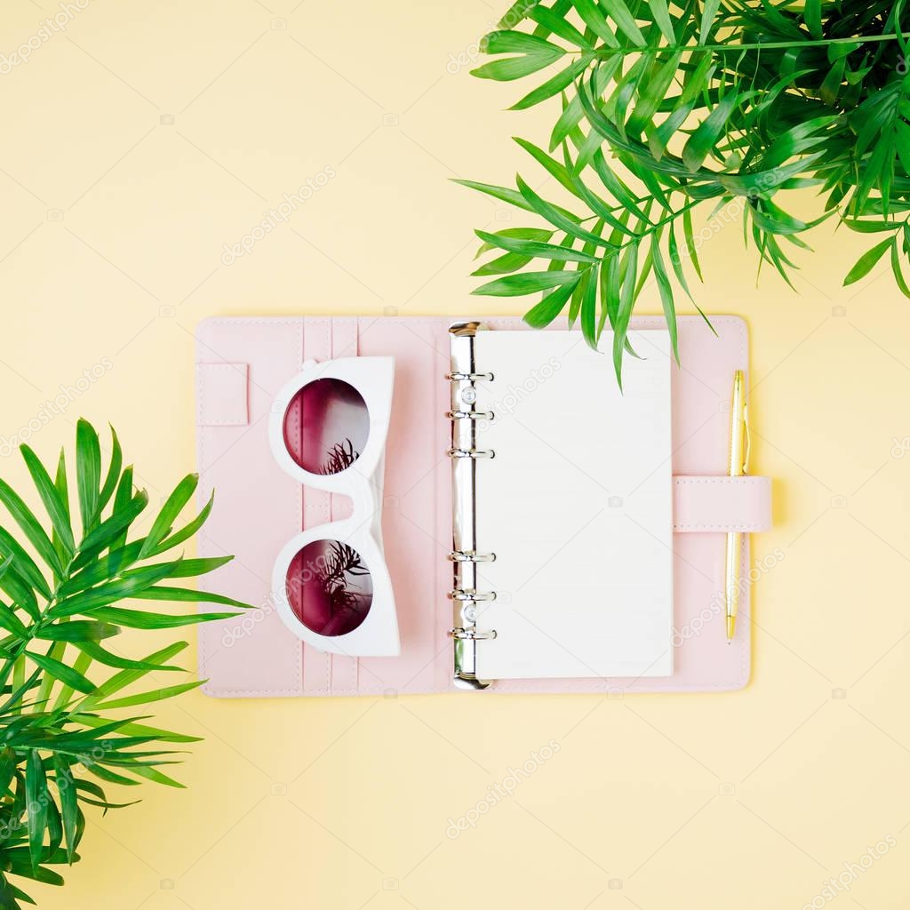 Tropical leaves, sunglasses, pink notebook on yellow background