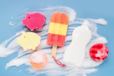 Bottle with washing agent and sponges on soapy foam background. Washing dishes concept. Flat lay, Top view.