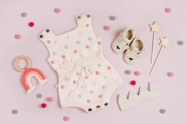 Cute set of baby clothes and accessories on pink background. Pastel knitted romper with jumper, shoes and toys. Fashion newborn bodysuit. Flat lay, top view