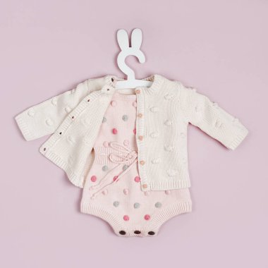 Pastel knitted romper with dots and cute jumper on hanger. Fashion newborn clothes on pink background. Flat lay, top view