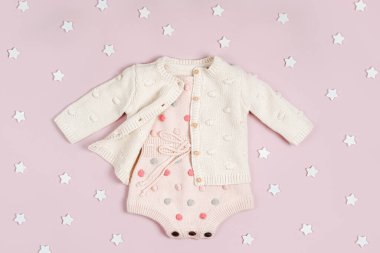 Fashion newborn clothes. Pastel knitted romper with dots and cute jumper  on pink background with stars.  Flat lay, top view