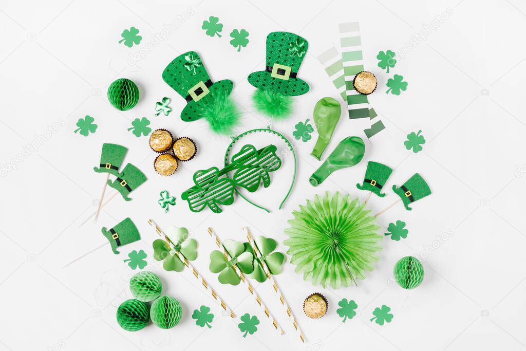 Decorations and props for St.Patrick 's Day party. Green and gold paper decorations, hair hoop with hats, clover leaf, sunglasses,  balloons, confetti and candy on white background. Flat lay, top view