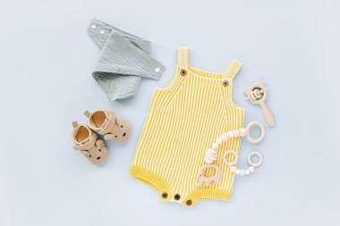 Yellow  knitted romper  wiht baby shoes, toys and accessories. Fashion newborn clothes on blue background. Flat lay, top view