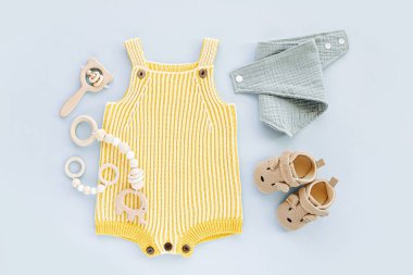 Yellow  knitted romper  wiht baby shoes, toys and accessories. Fashion newborn clothes on blue background. Flat lay, top view