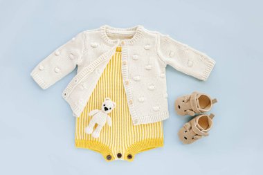 Yellow  knitted romper and jumper  wiht baby shoes and toys on blue background. Fashion newborn clothes. Flat lay, top view