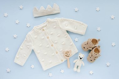 Pastel knitted jumper, cotton crown and baby shoes. Cute set of baby clothes and accessories for little prince on blue background.  Fashion newborn. Flat lay, top view