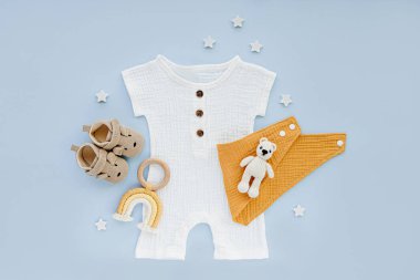 White cotton bodysuit with baby shoes and toys. Set of baby clothes and accessories on blue background. Fashion newborn clothes for summer. Flat lay, top view