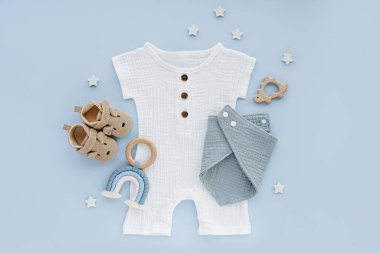White cotton bodysuit with baby shoes and toys. Set of baby clothes and accessories on blue background. Fashion newborn clothes for summer. Flat lay, top view