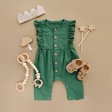 Green romper  with   wooden toys and baby shoes. Set of baby clothes and accessories on beige background.  Fashion newborn. Flat lay, top view