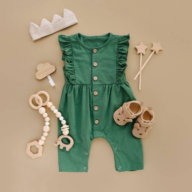 Green romper  with   wooden toys and baby shoes. Set of baby clothes and accessories on beige background.  Fashion newborn. Flat lay, top view clipart