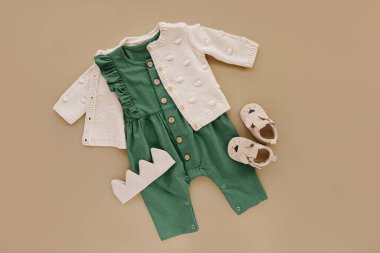 Green romper  with knitted  jumper, cotton crown and baby shoes. Set of baby clothes and accessories on beige background.  Fashion newborn. Flat lay, top view